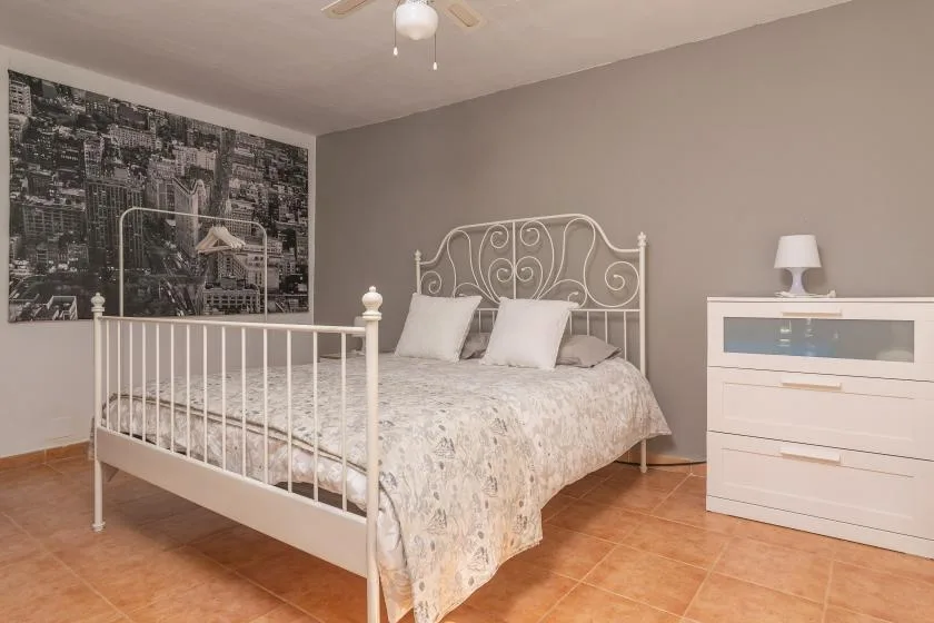 A bedroom with a bed, a white dresser, and a large cityscape wall print.