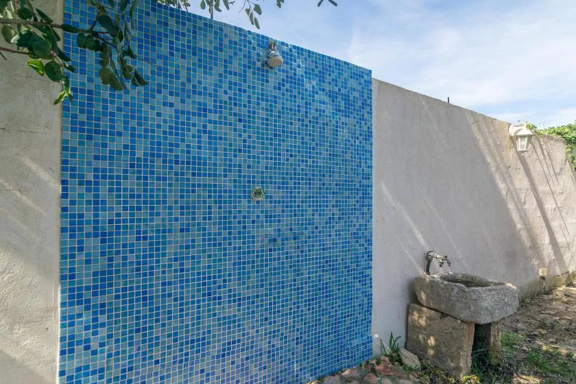An outdoor shower area has a blue tiled wall and a stone basin.