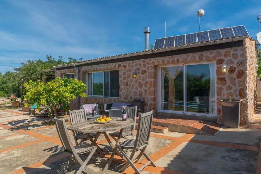 A stone house opens onto a sunny patio with an outdoor dining table and chairs.