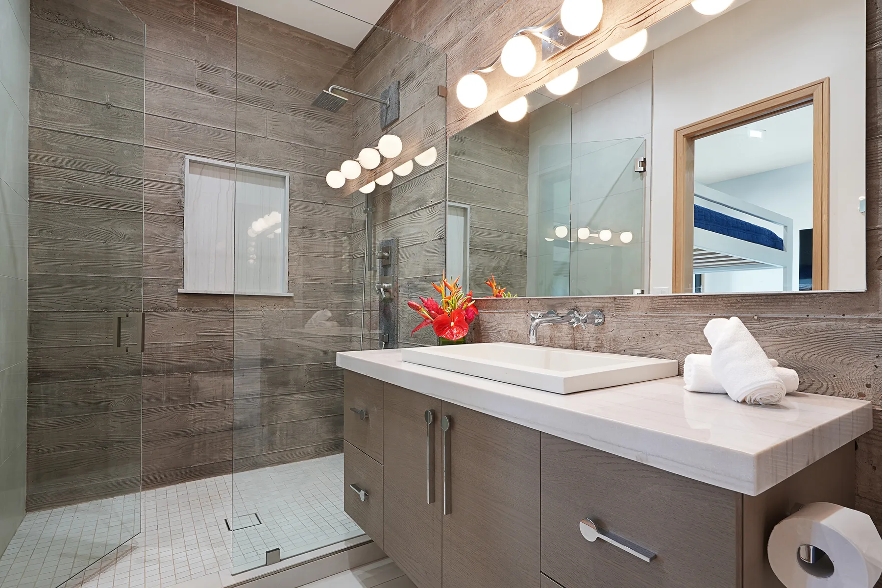 A bathroom vanity with a broad mirror and glass shower.