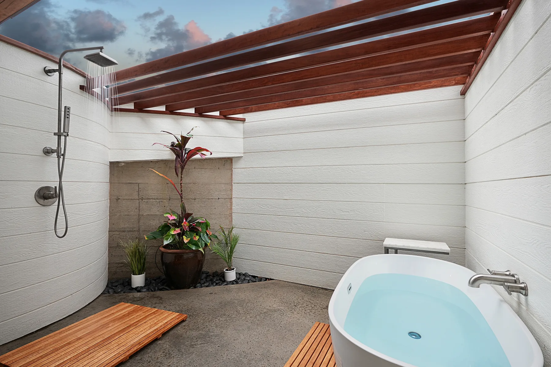 An outdoor bathing area with a shower, soaking tub, and wooden overhead slats.