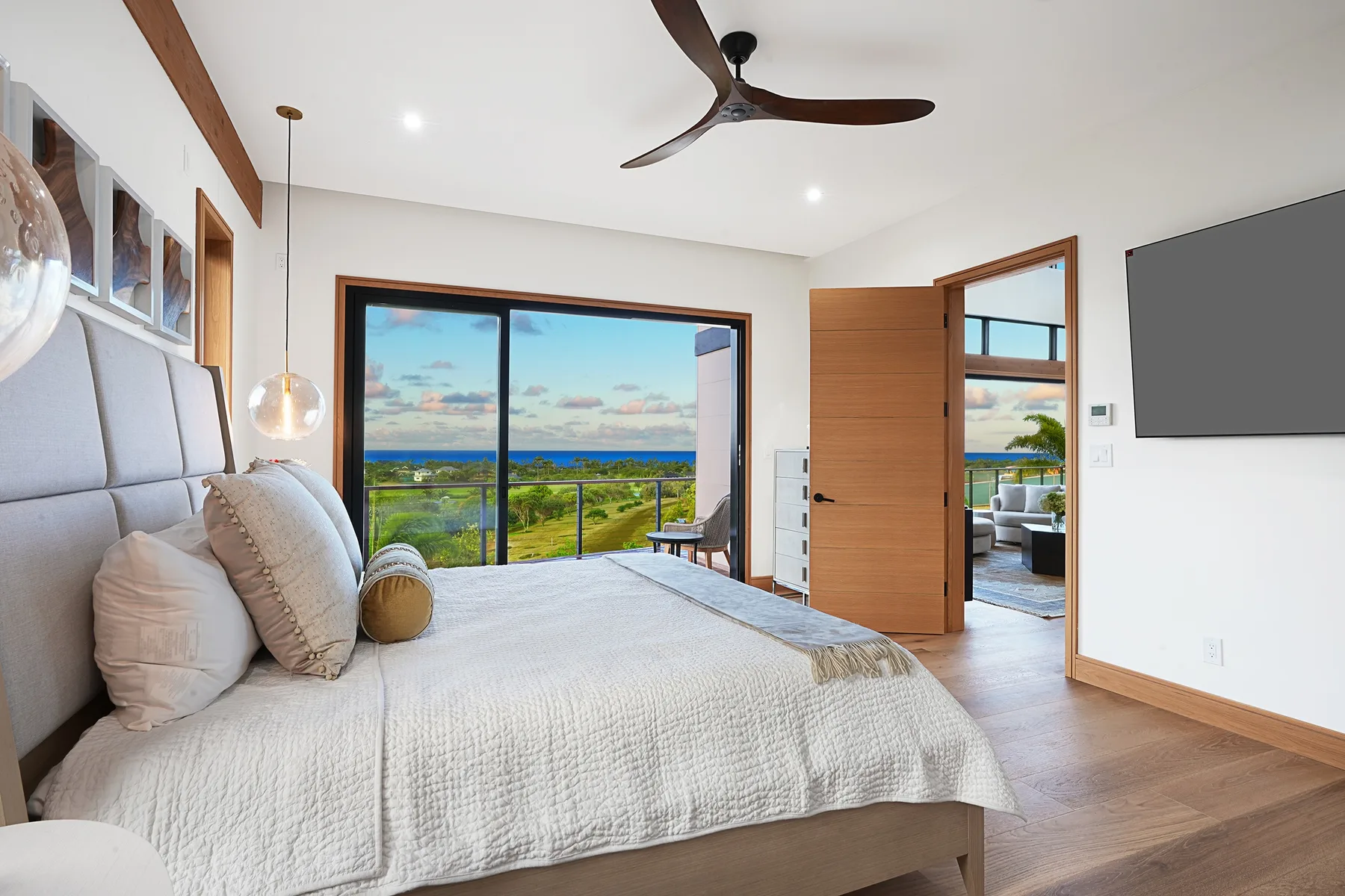A bright bedroom with a large bed and wide windows overlooking greenery and the sea.