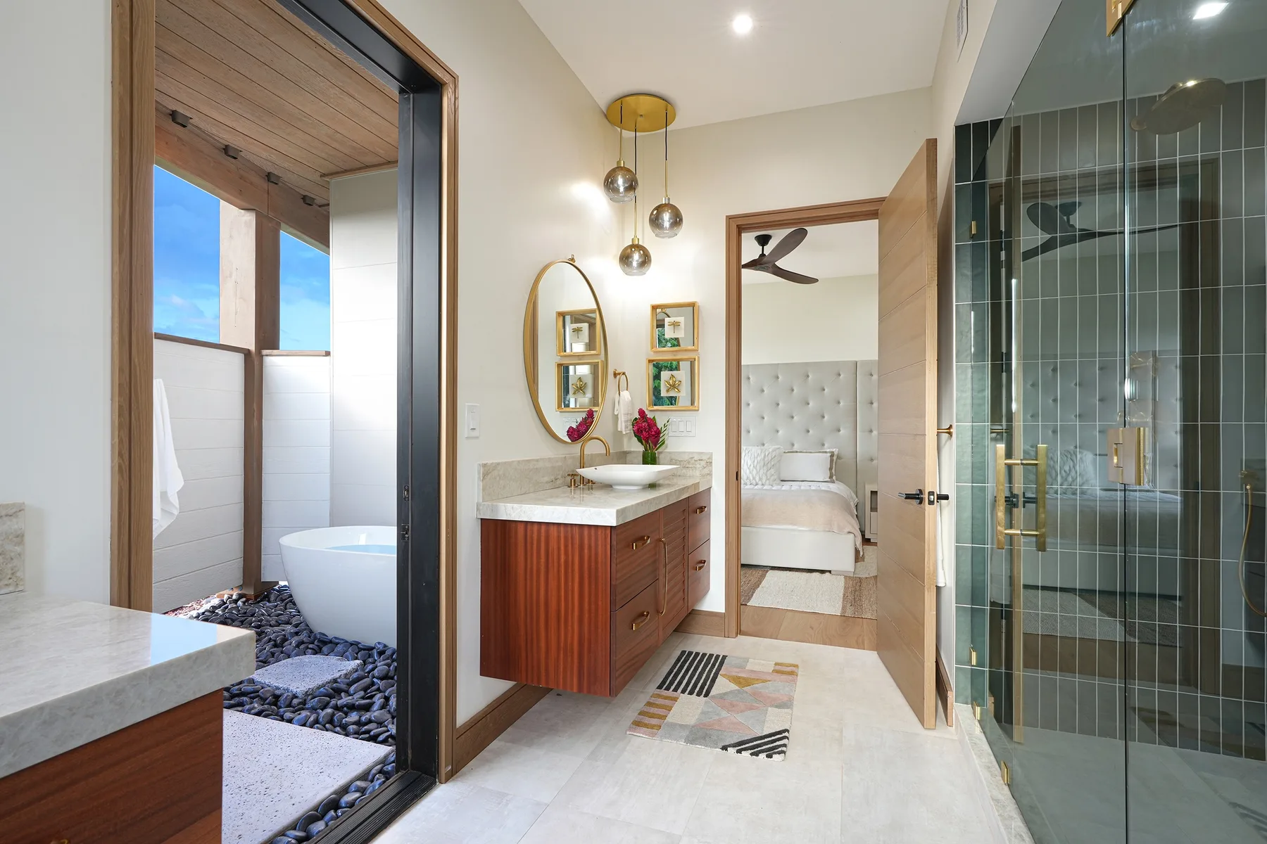 A bathroom vanity and glass shower stand beside an open doorway to a bedroom.