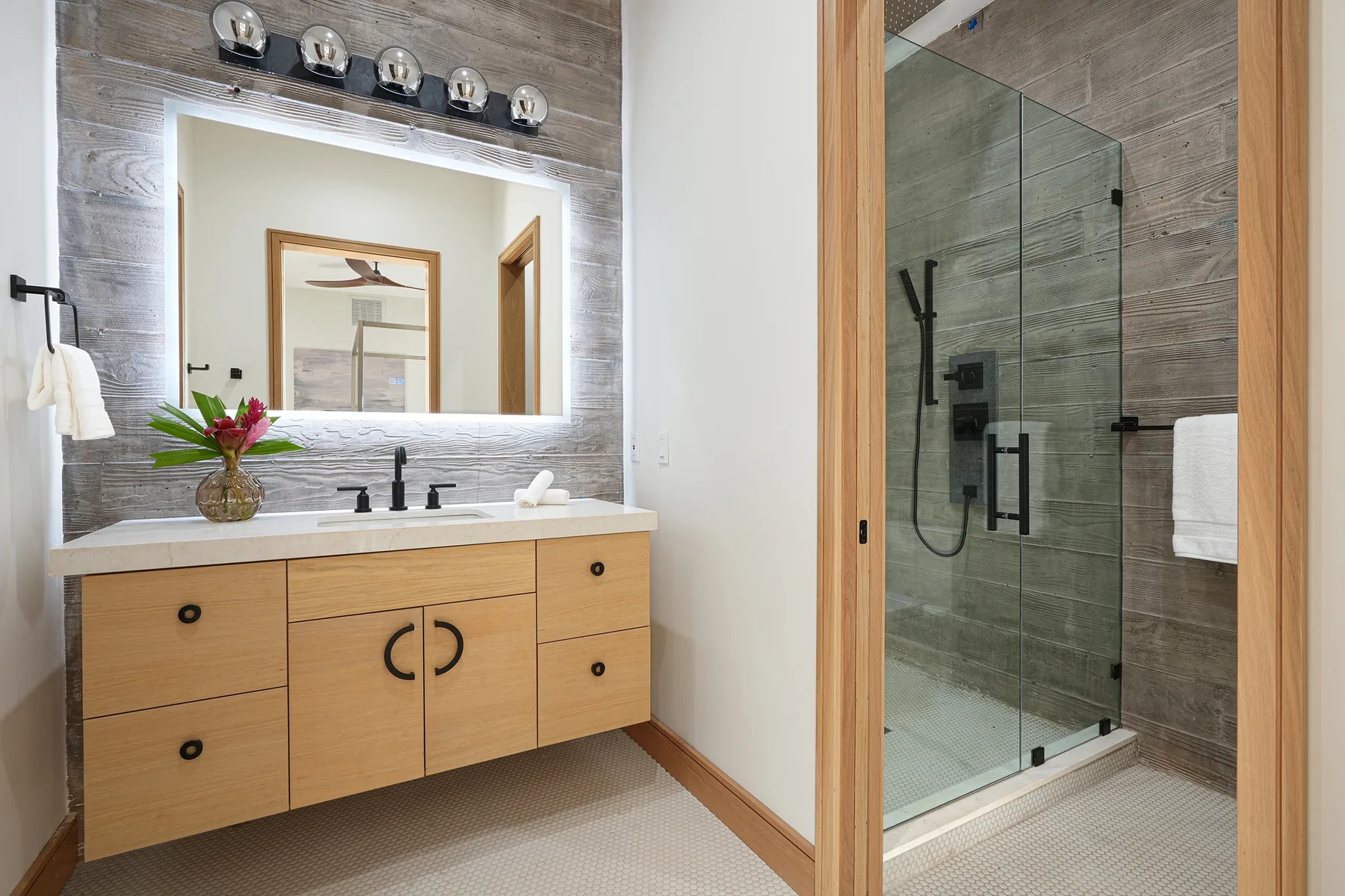 A bathroom vanity with a large mirror stands beside a glass-enclosed shower.