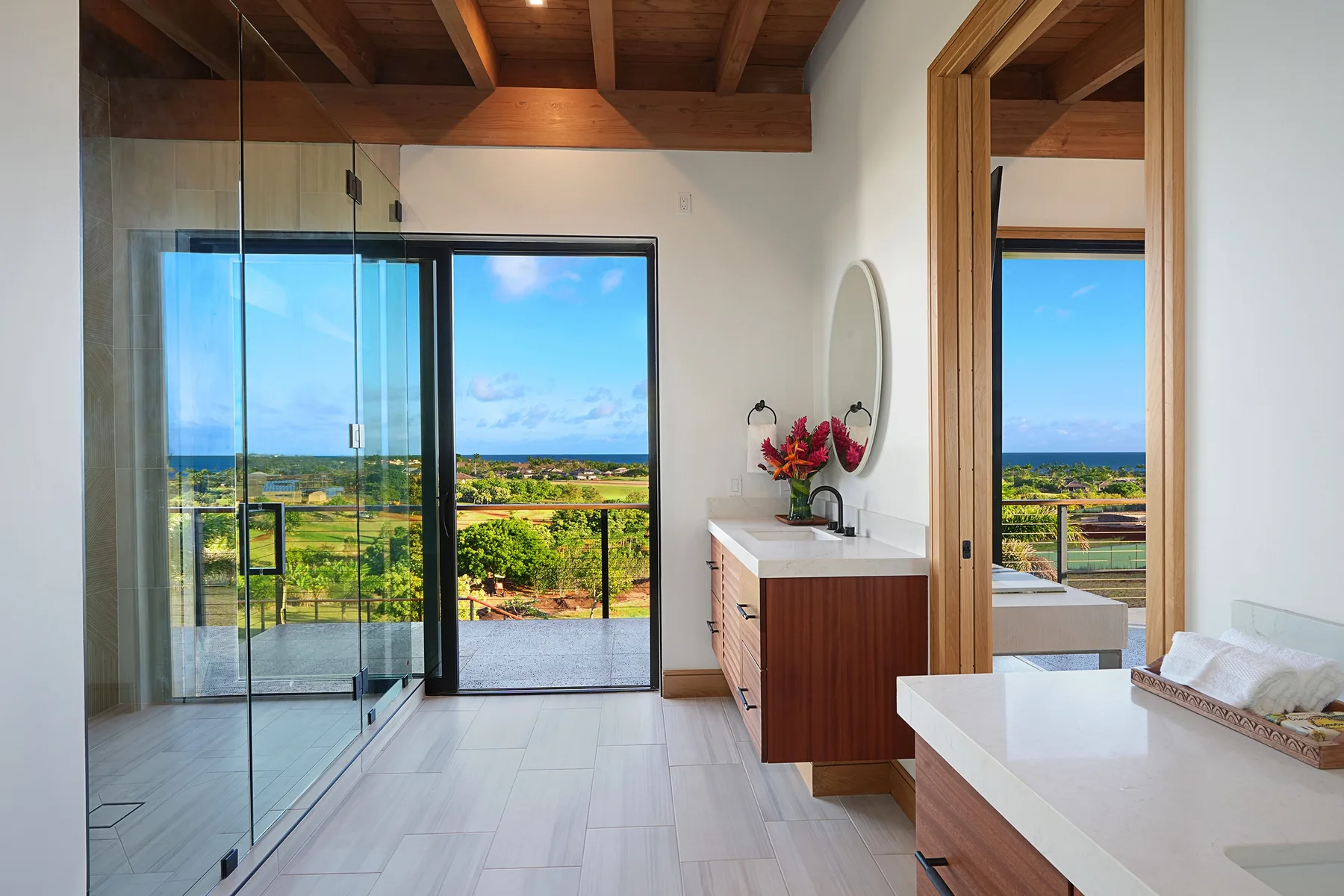 A bright bathroom opens onto a balcony with views of the sea and greenery.