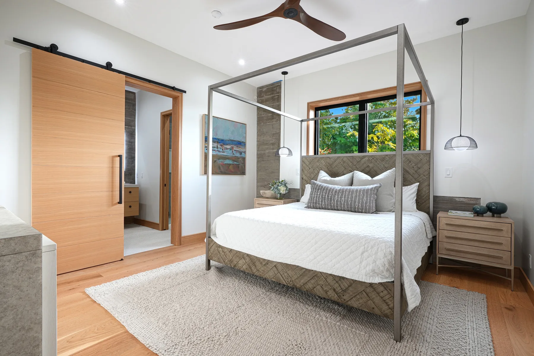 A bright bedroom with a large bed, a window, and light wood flooring.