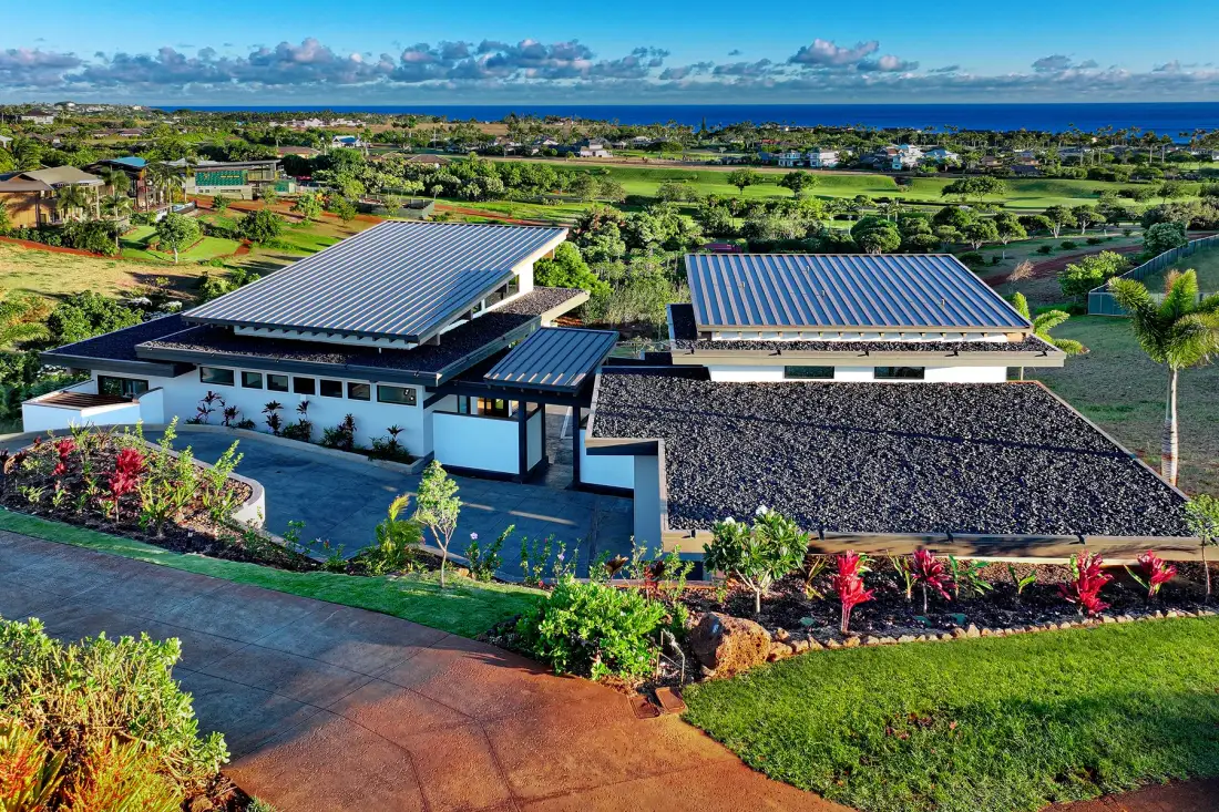 A modern building sits among landscaped gardens, with the ocean visible in the distance.