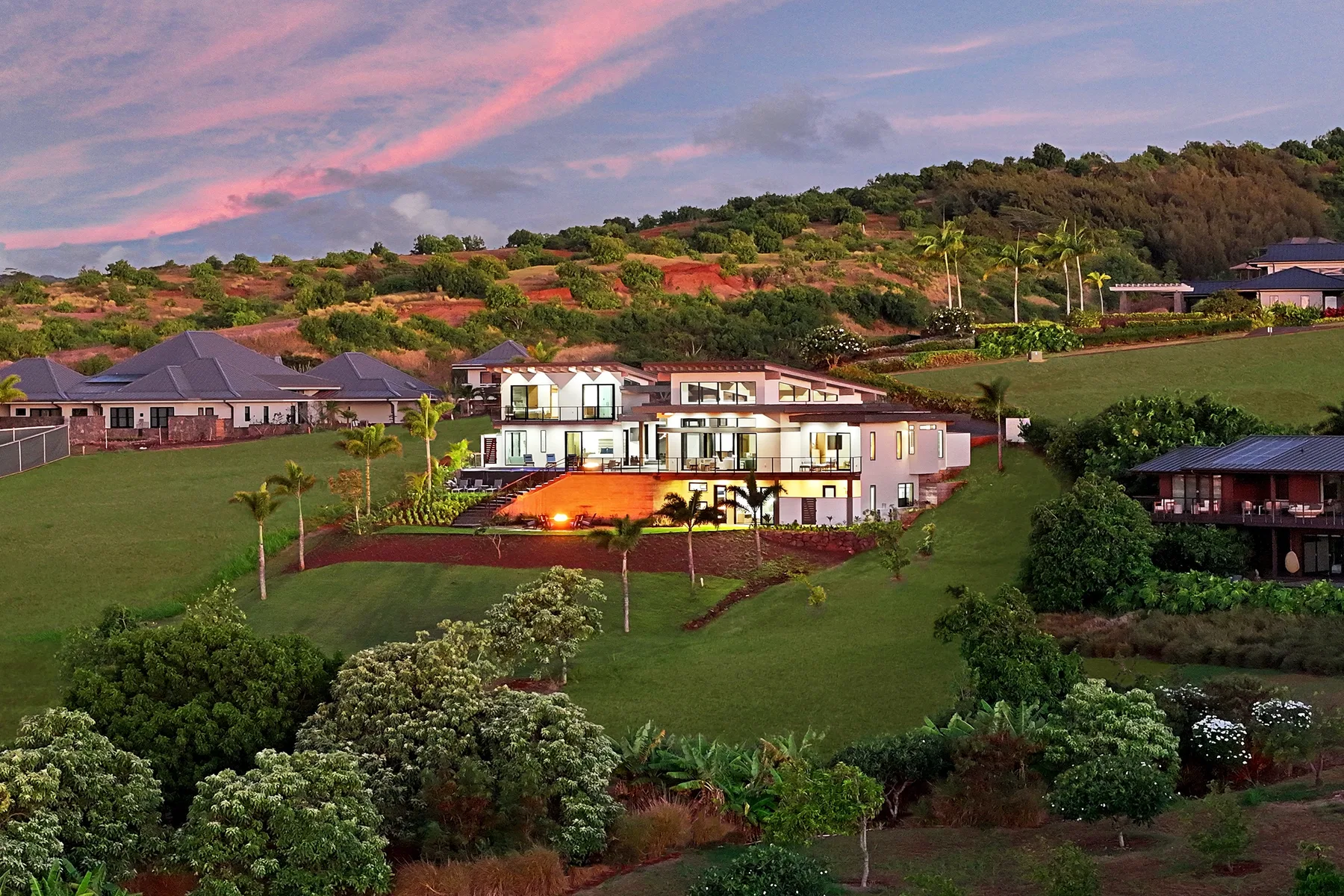Hillside homes overlook a landscaped green slope beneath a pink evening sky.