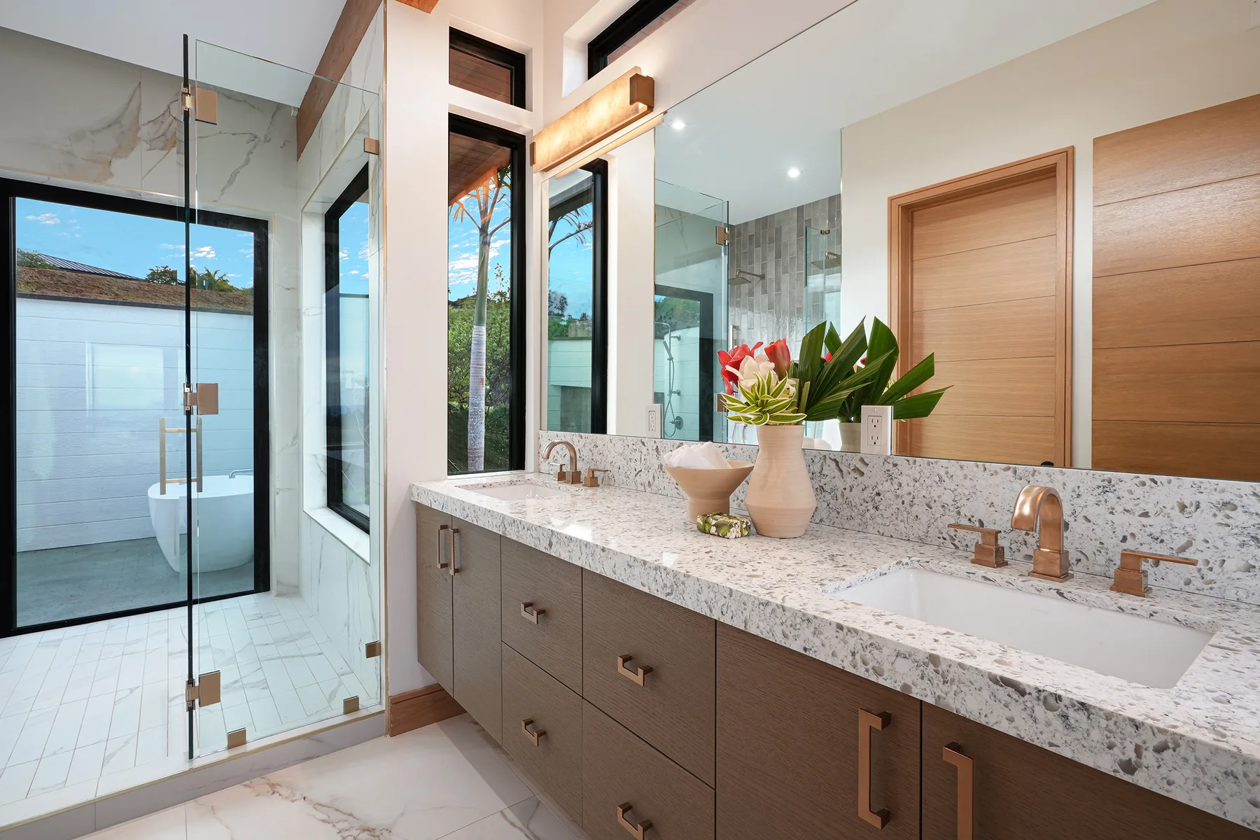 A bright bathroom with a glass shower and a long vanity topped with a sink.