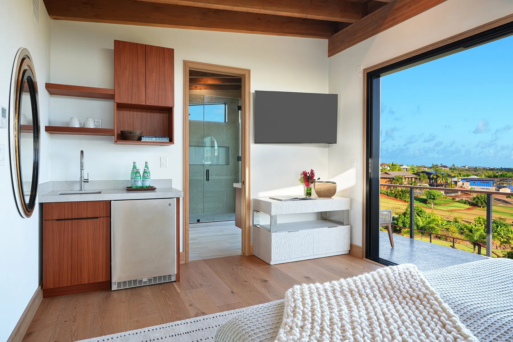 A bright bedroom with a bed, a small desk, and a large balcony window.