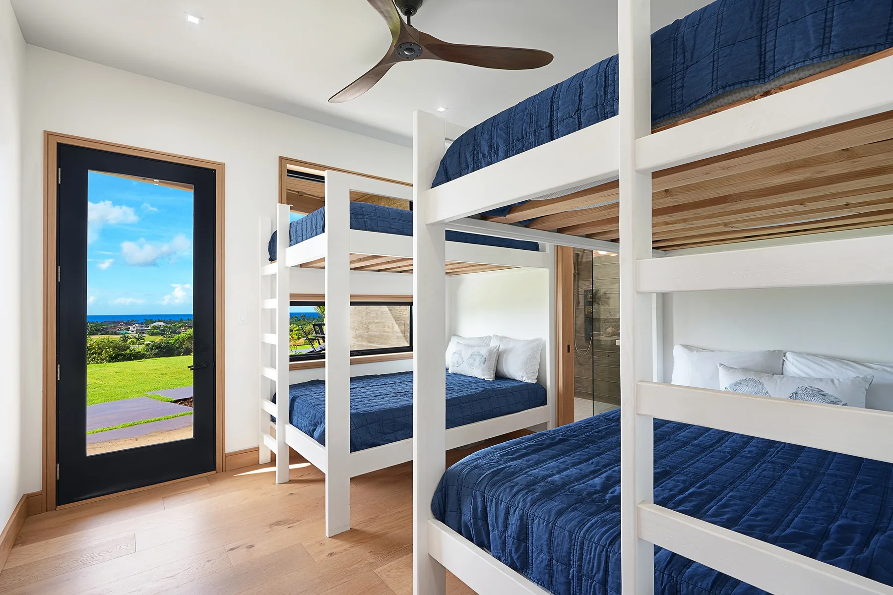 A bunk bedroom with white bunk beds and blue bedding beside a glass door.