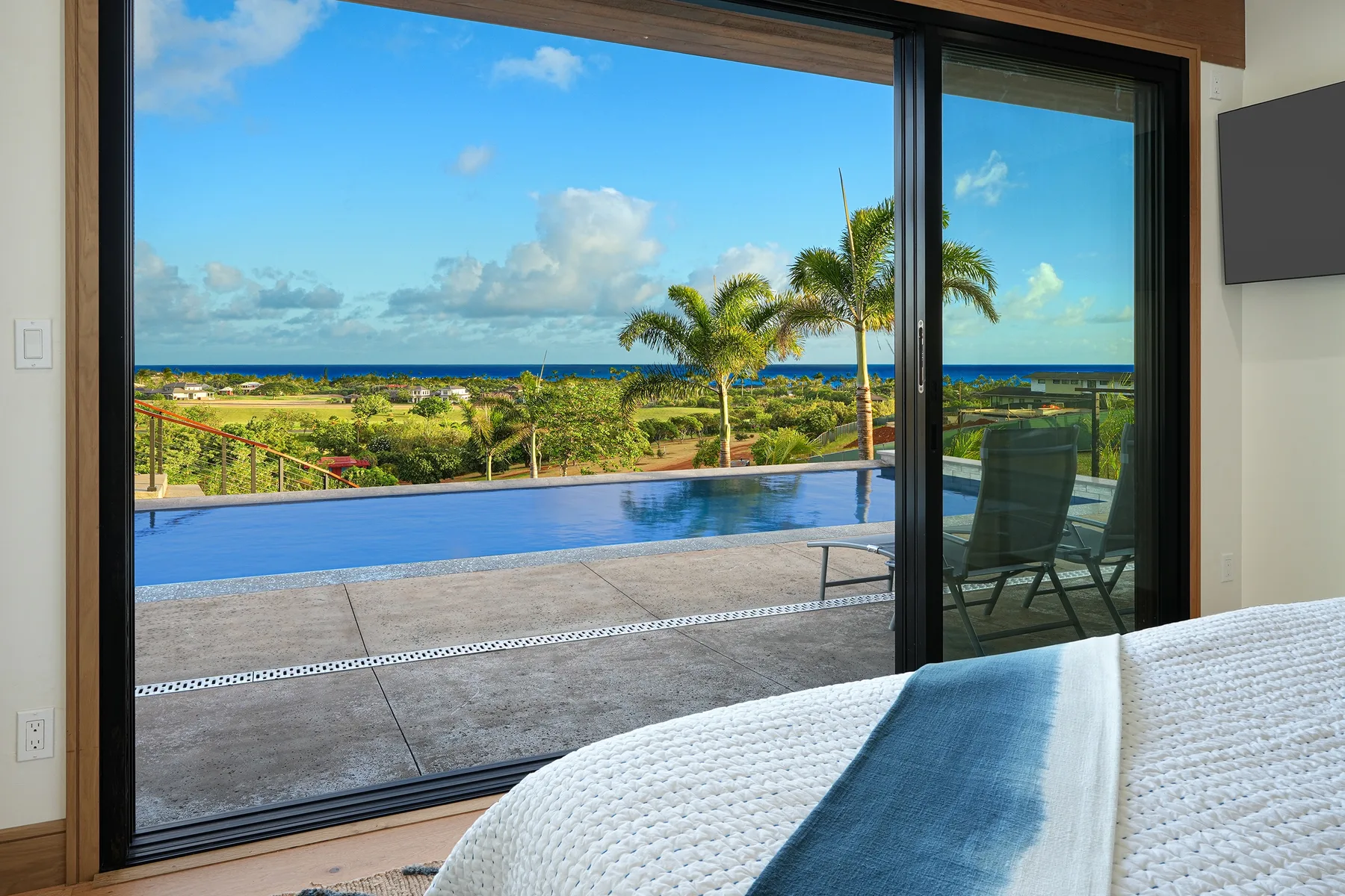 A bedroom opens onto a terrace with a pool and ocean views.