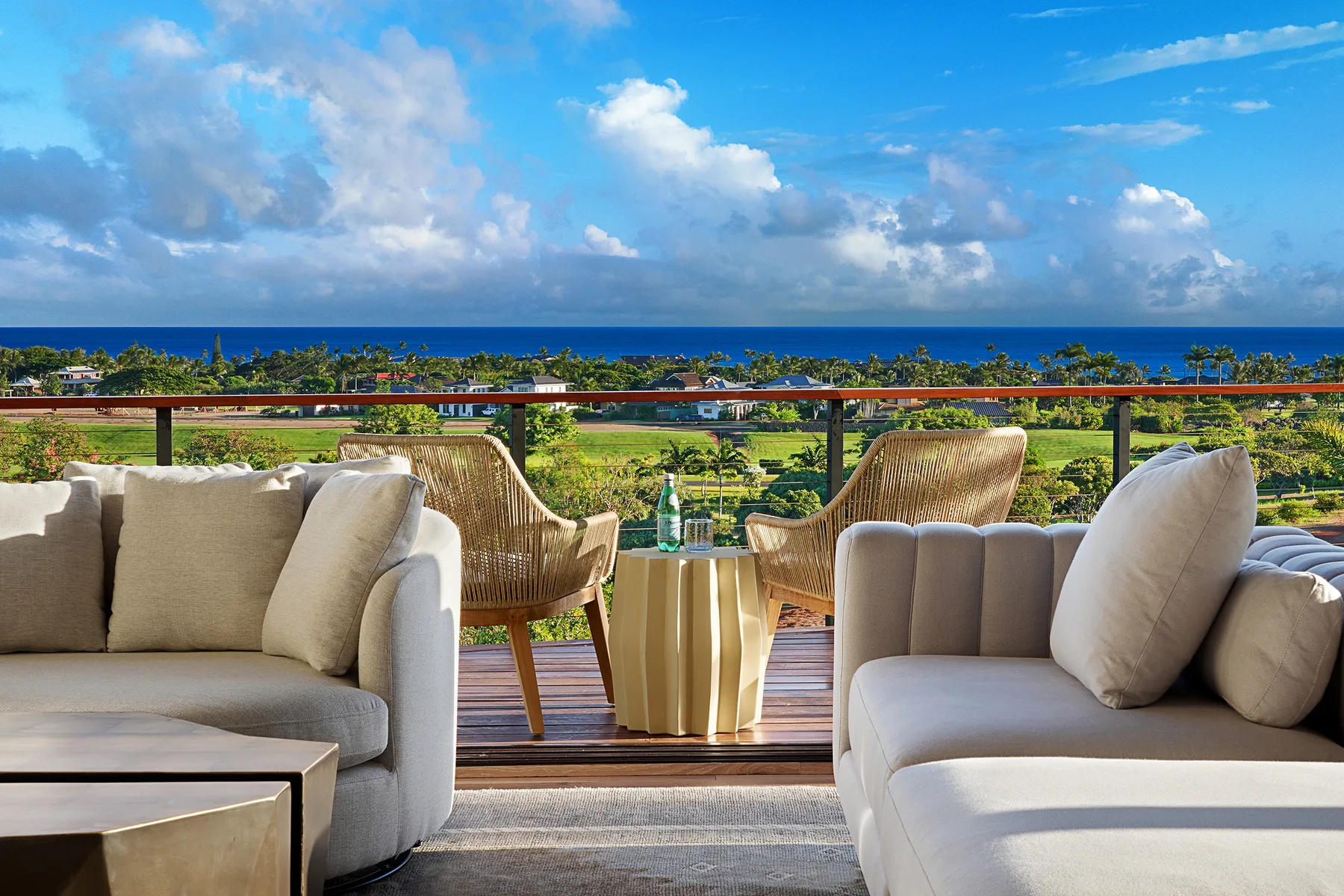 Outdoor seating overlooks a green landscape and the ocean beneath a cloudy sky.