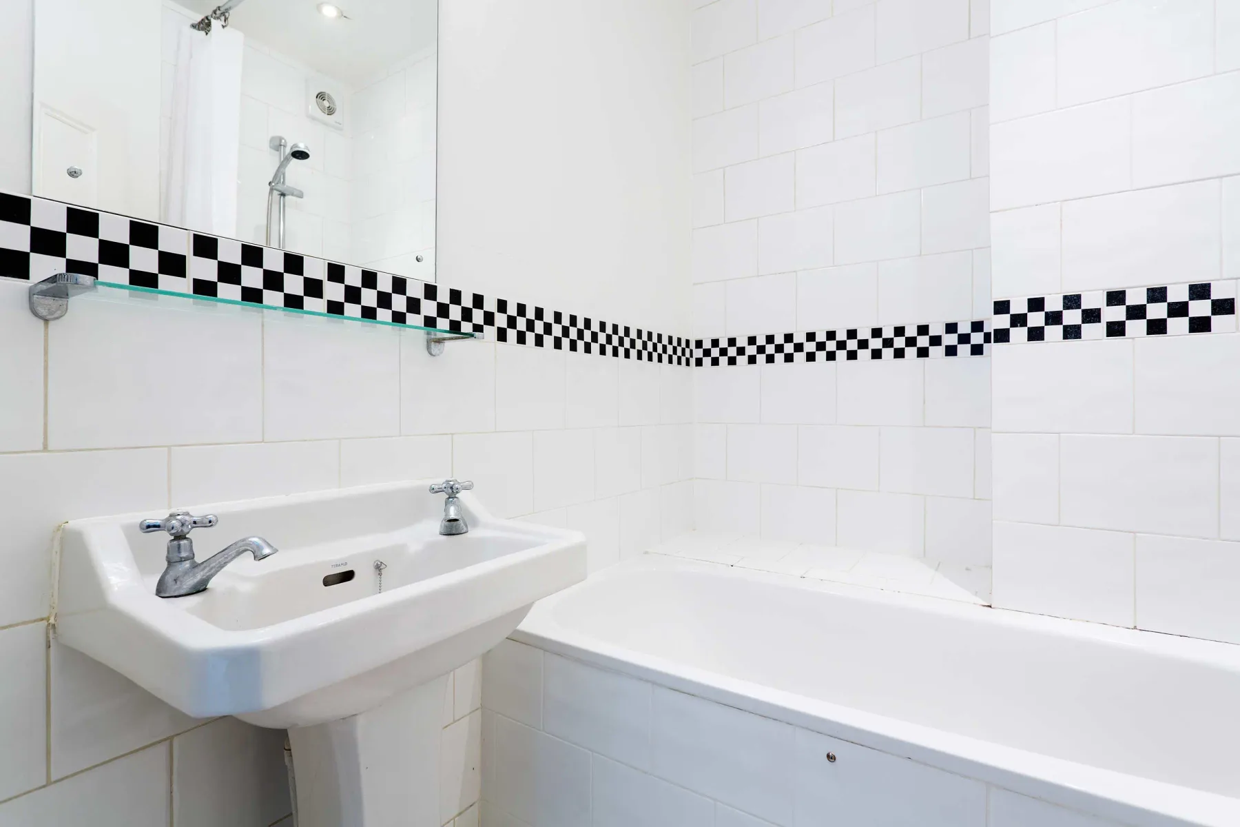 A tiled bathroom with a sink, bathtub, and black-and-white wall border.