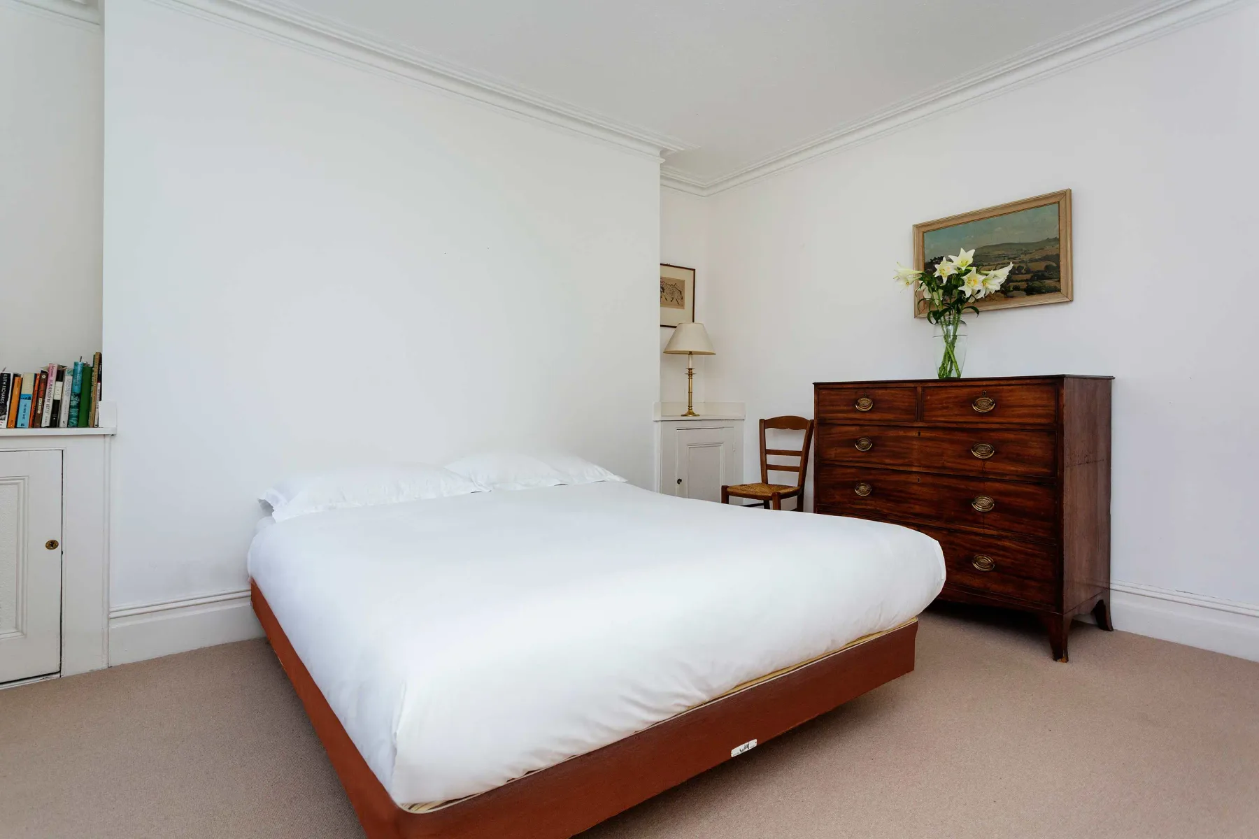 A bright bedroom with a large bed and a wooden chest of drawers.