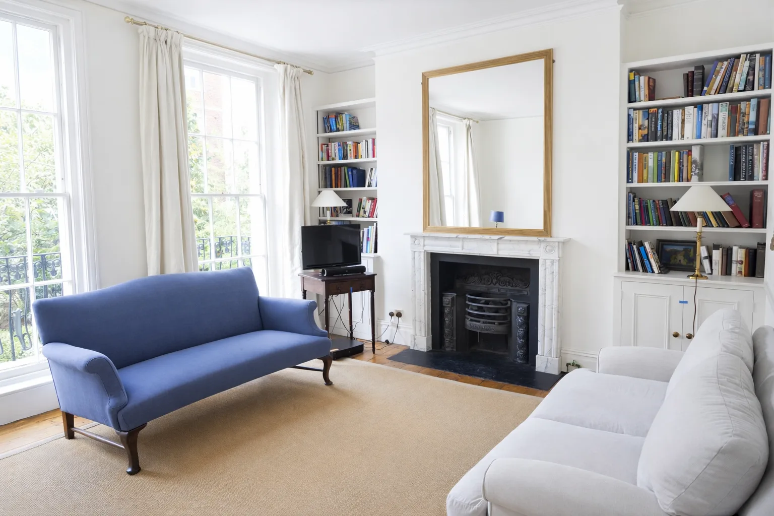 A bright living room with blue and white seating, bookshelves, and a fireplace.