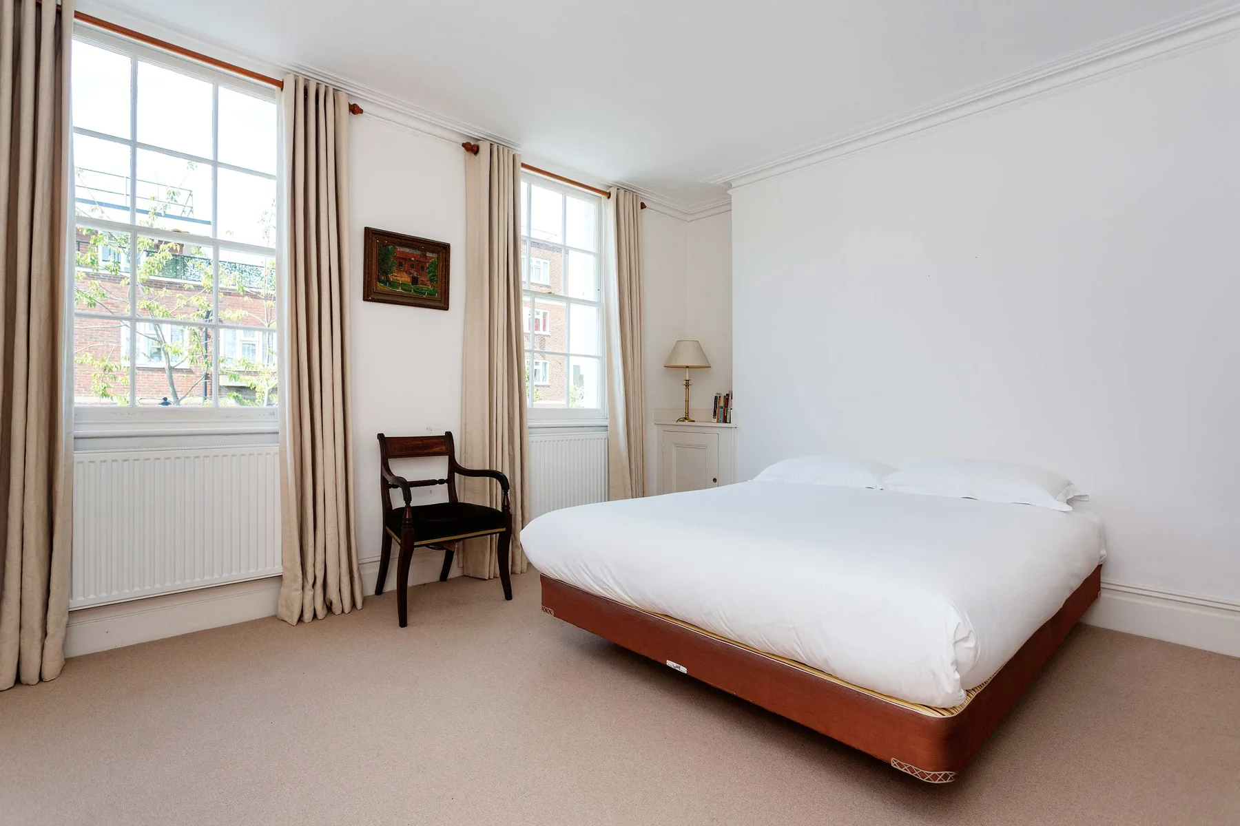 A bright bedroom with a bed beside tall windows and a chair.