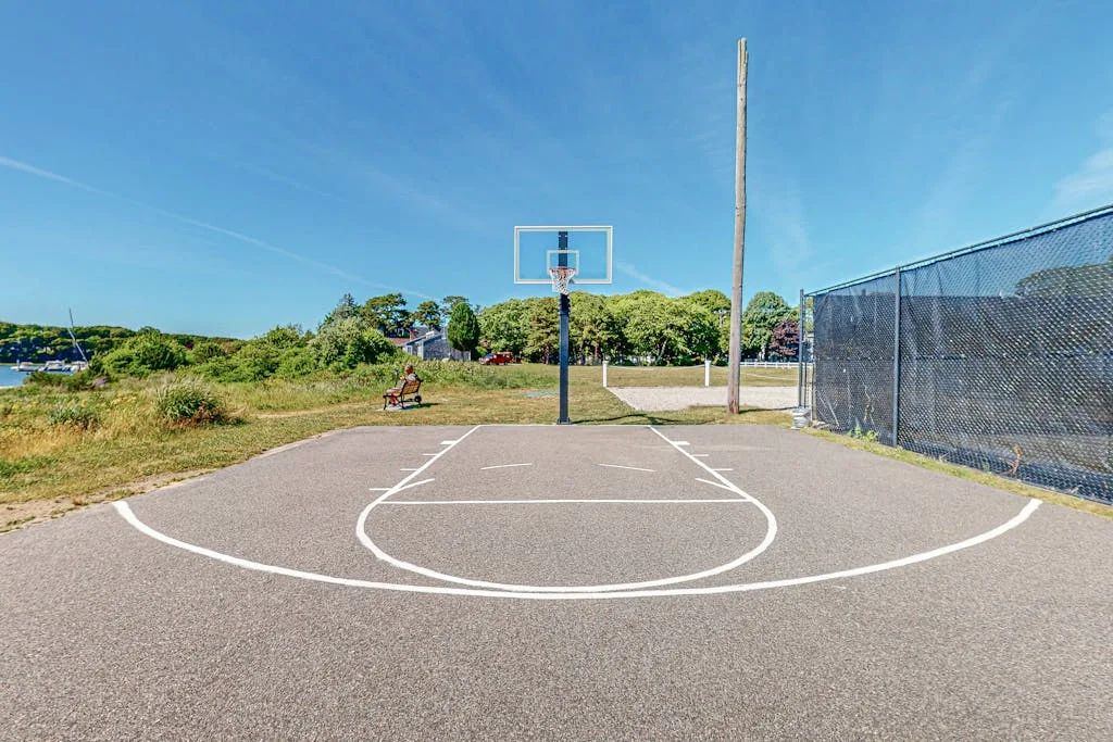 Una cancha de baloncesto al aire libre con una canasta y una valla metálica.