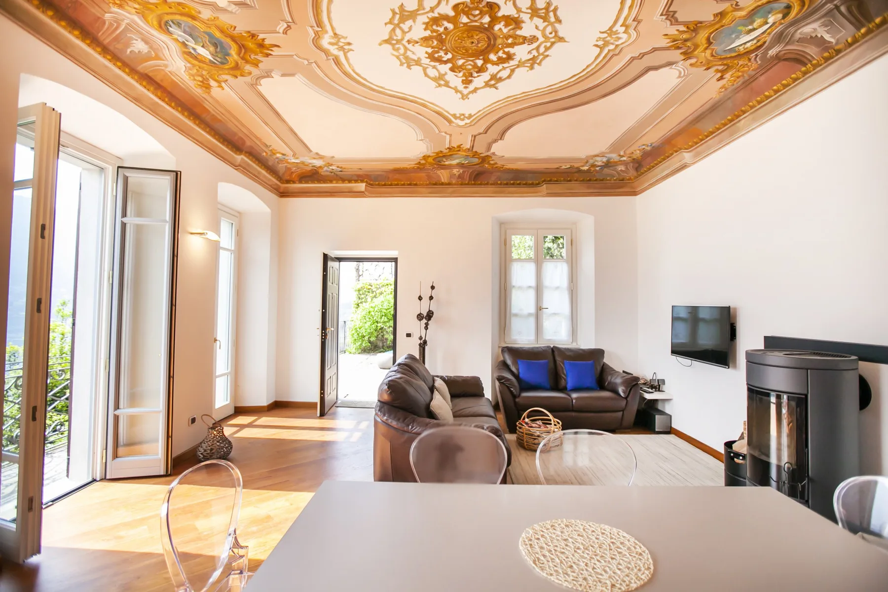 A bright living room with seating, a television, and an ornate painted ceiling.
