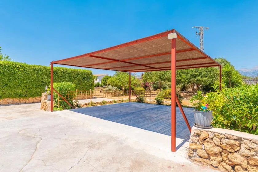 A covered outdoor area with a paved surface and surrounding garden greenery.