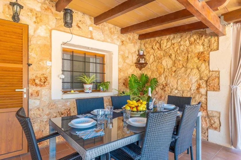 A dining area with a glass table and dark woven seating beside stone walls.