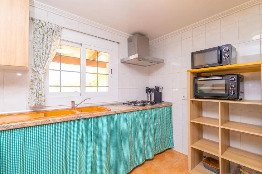 A tiled kitchen with a sink, stovetop, and open wooden shelving.