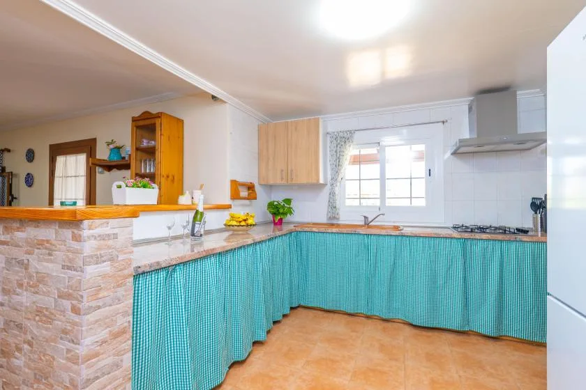 A bright kitchen with turquoise curtains beneath the counters and a window above the sink.