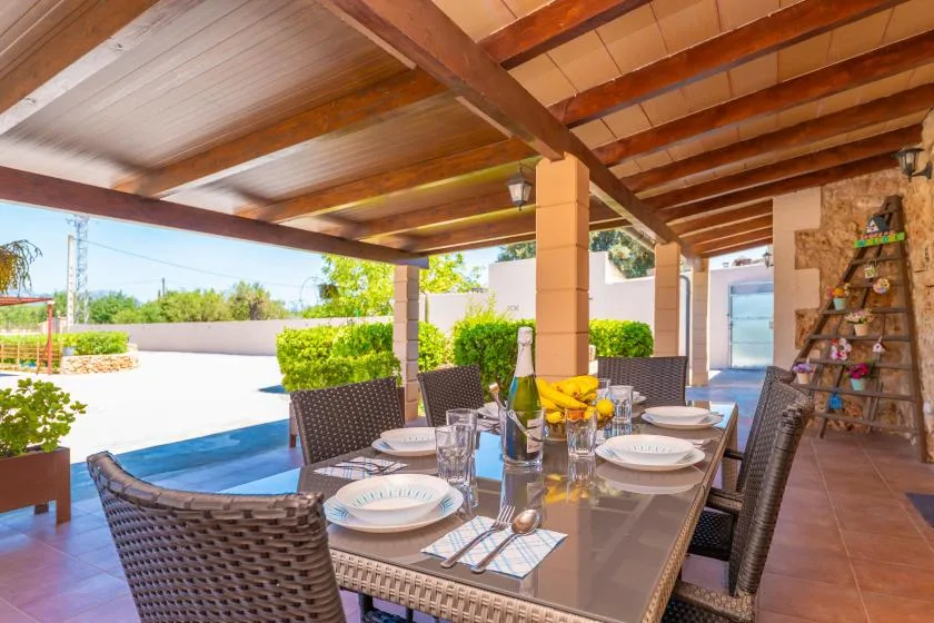 A covered outdoor dining area with a set table beside a swimming pool.