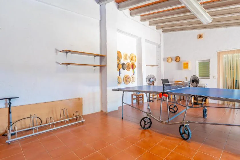 A bright indoor recreation room with a table tennis table and wall-mounted shelves.
