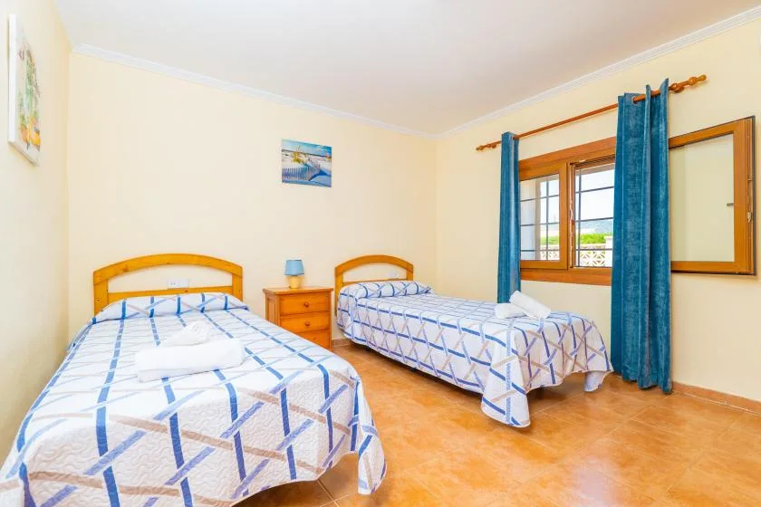 A bedroom with two beds, patterned bedding, and blue curtains by the window.