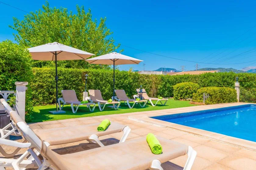 An outdoor swimming pool is surrounded by loungers, umbrellas, and greenery.