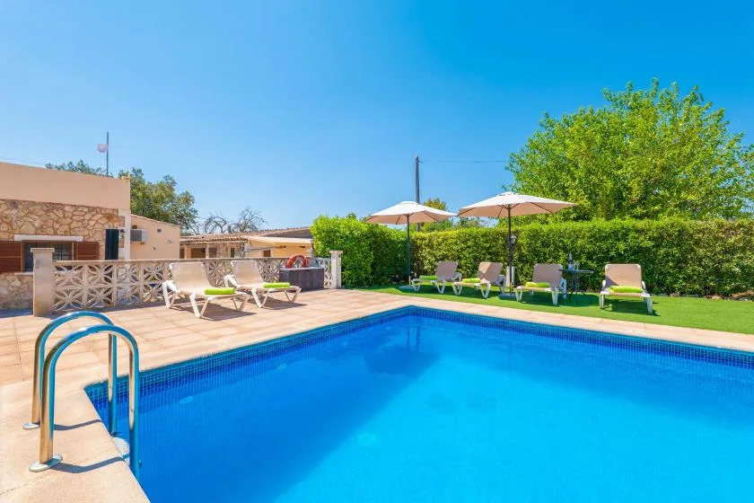 A swimming pool beside a sun deck with lounge seating and umbrellas.