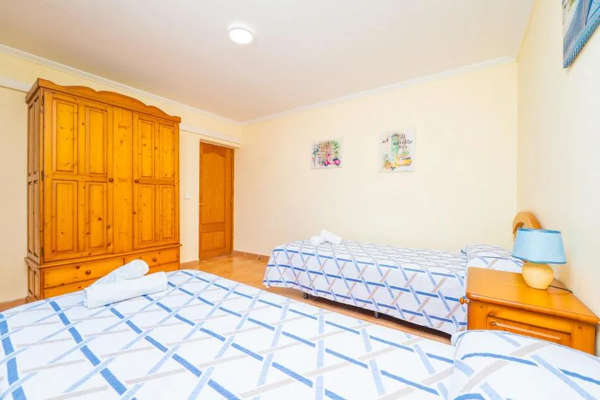 A bedroom with two beds, a wooden wardrobe, and a bedside table.
