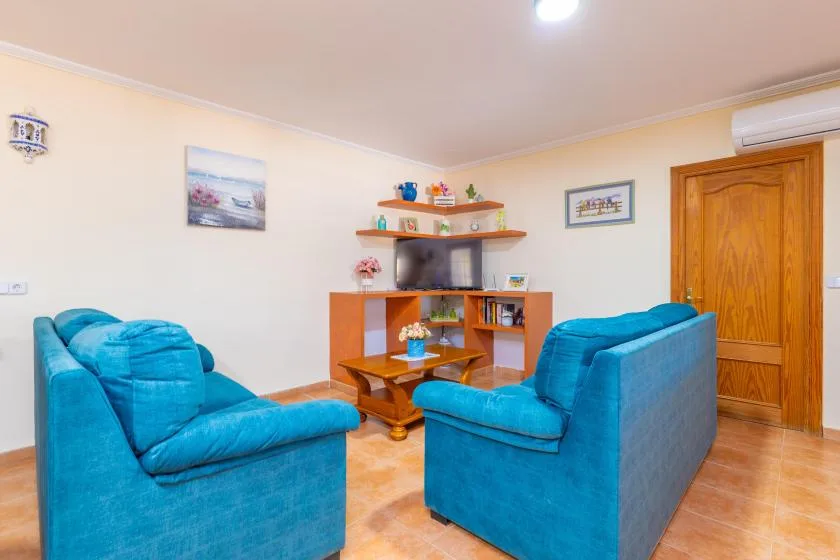 A living room with blue seating arranged around a television and wooden shelves.