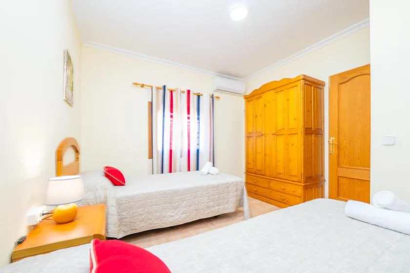 A bright bedroom with two beds and wooden wardrobes.