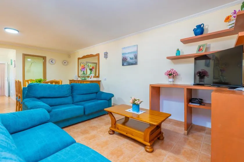 A living room with blue seating, a wooden coffee table, and a television.