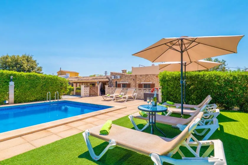 An outdoor pool and patio with lounge seating beneath a large umbrella.