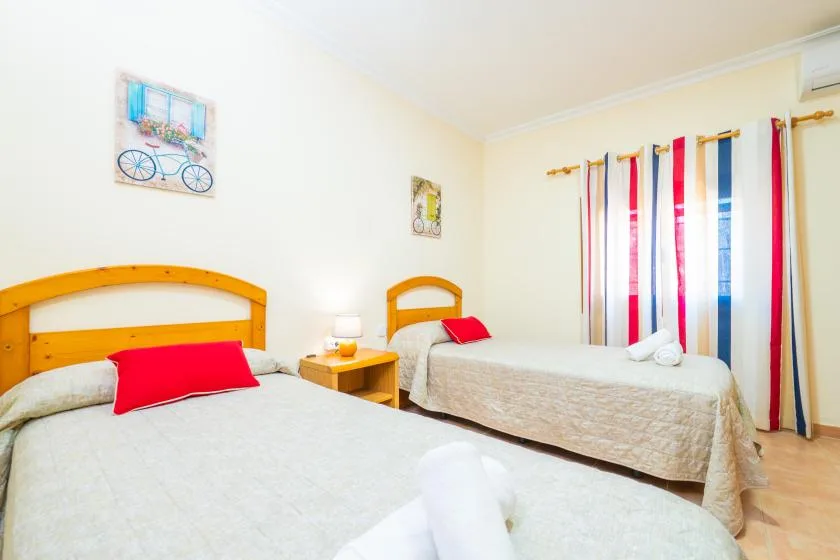 A bedroom with two beds, colorful curtains, and a small bedside table.