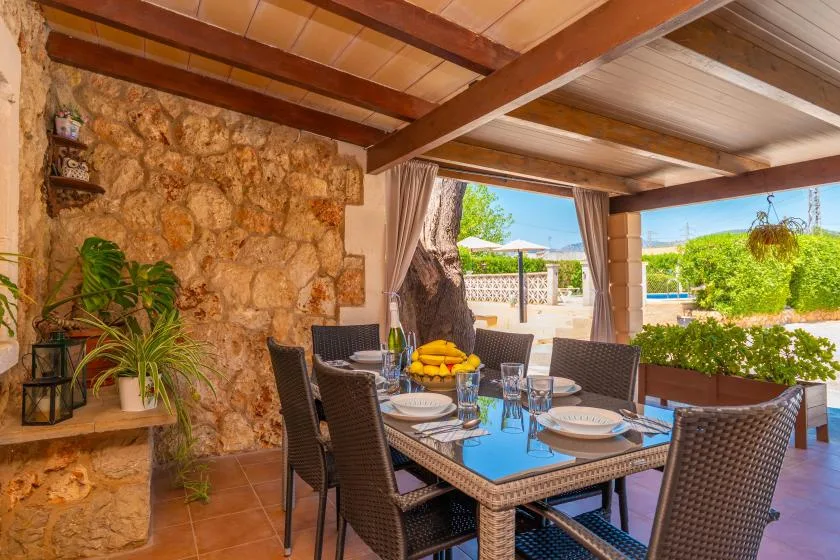 A covered patio dining area with a table set beside a stone wall.
