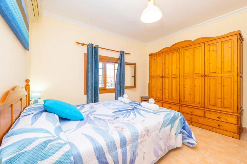 A bedroom with a bed covered in blue-and-white bedding and a large wooden wardrobe.