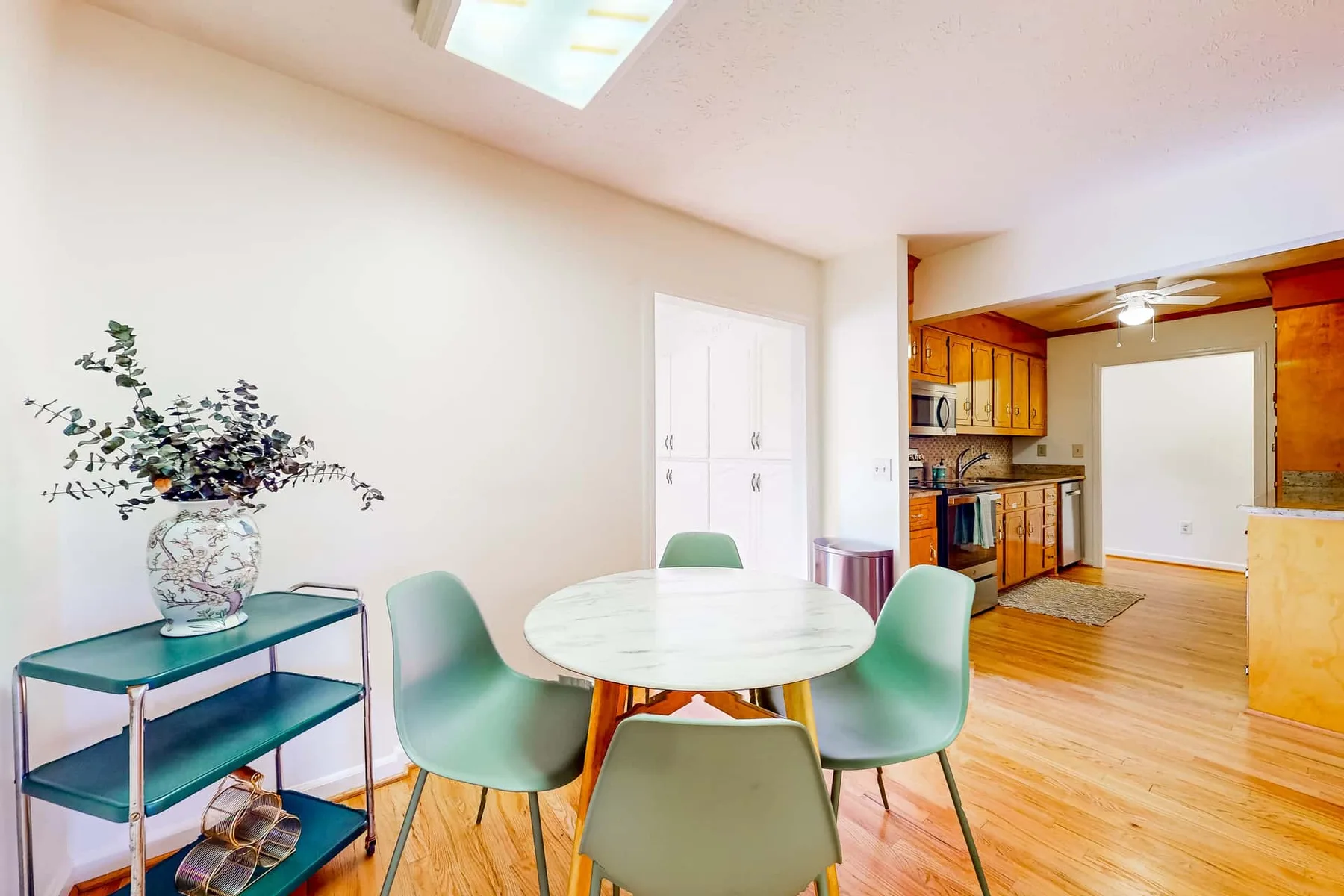 A dining area with a round table and green seating opens onto a kitchen.