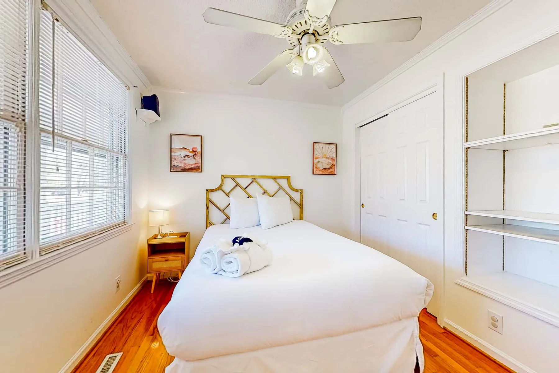 A bright bedroom with a bed, a ceiling fan, and windows with blinds.