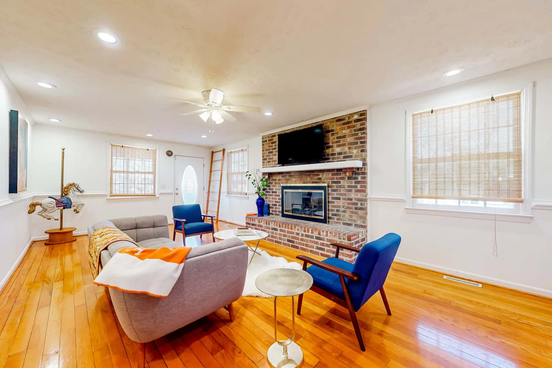 A bright living room with seating arranged around a brick fireplace and television.