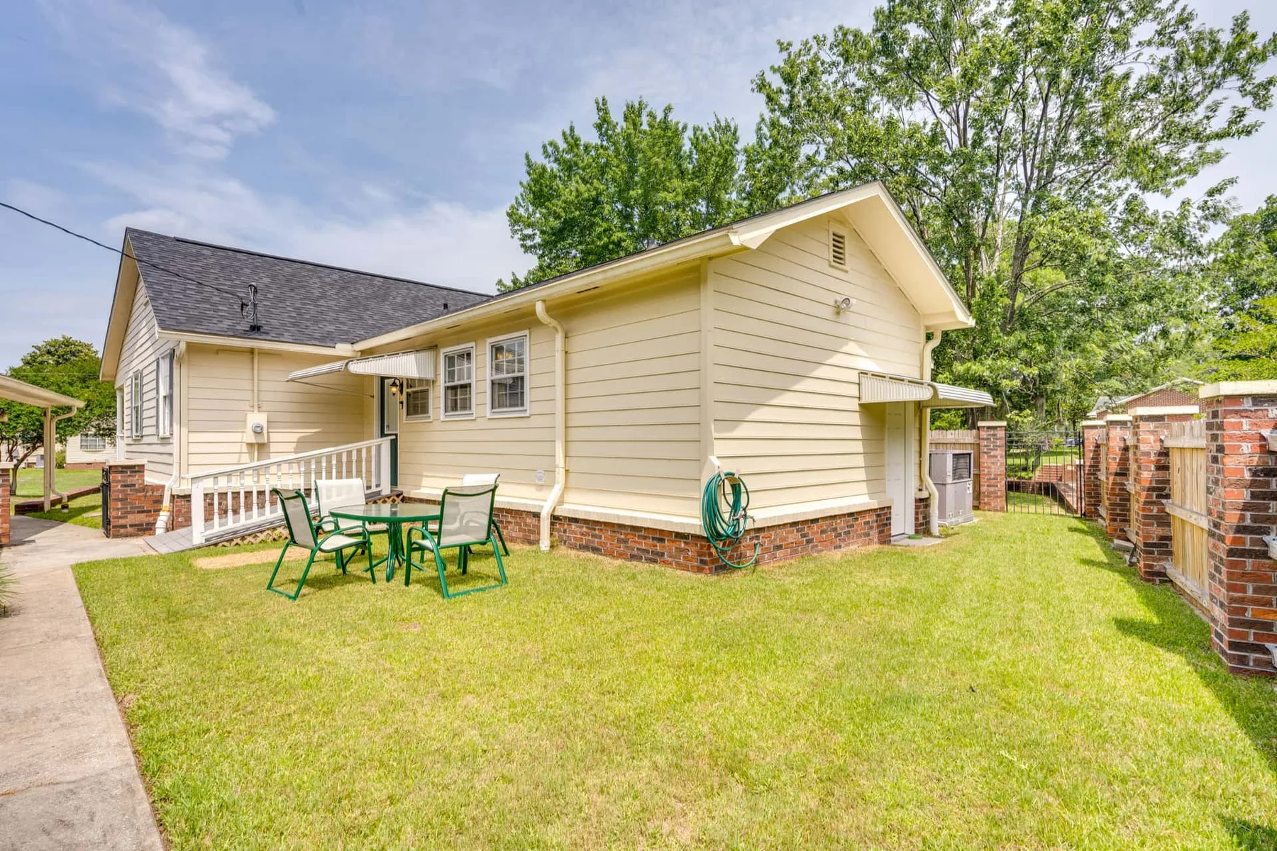 A light-colored house stands beside a grassy yard with outdoor seating.