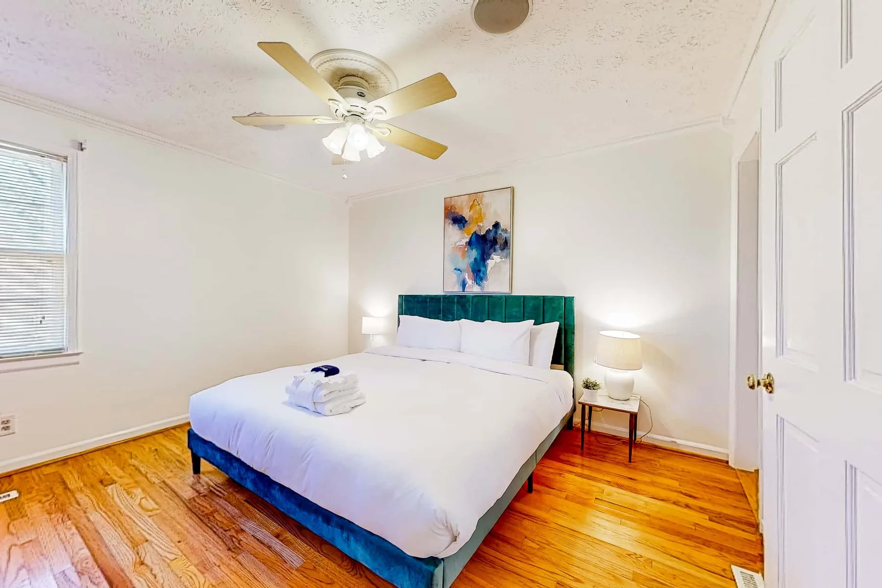 A bedroom with a neatly made bed and colorful artwork above the headboard.