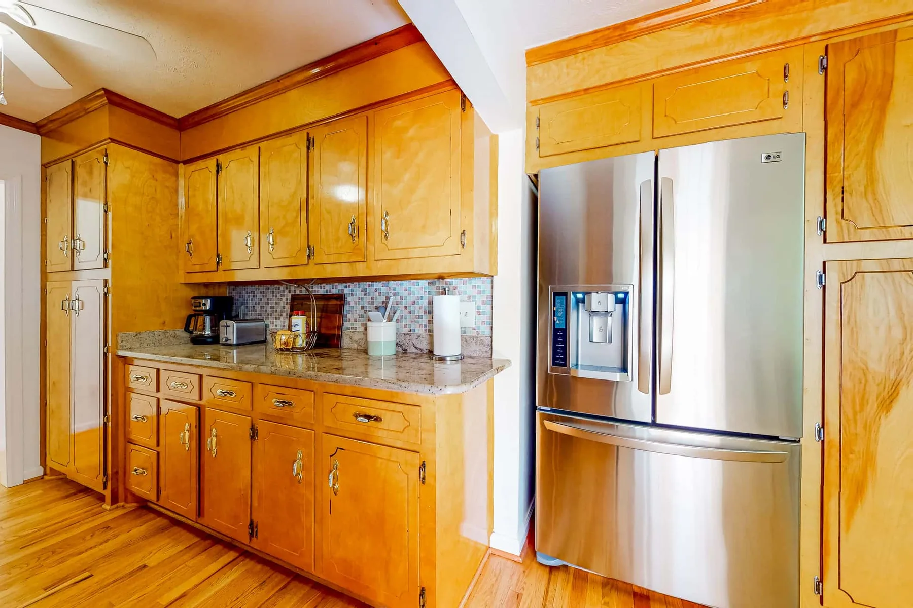 A kitchen with wooden cabinets, a tiled backsplash, and a stainless steel refrigerator.