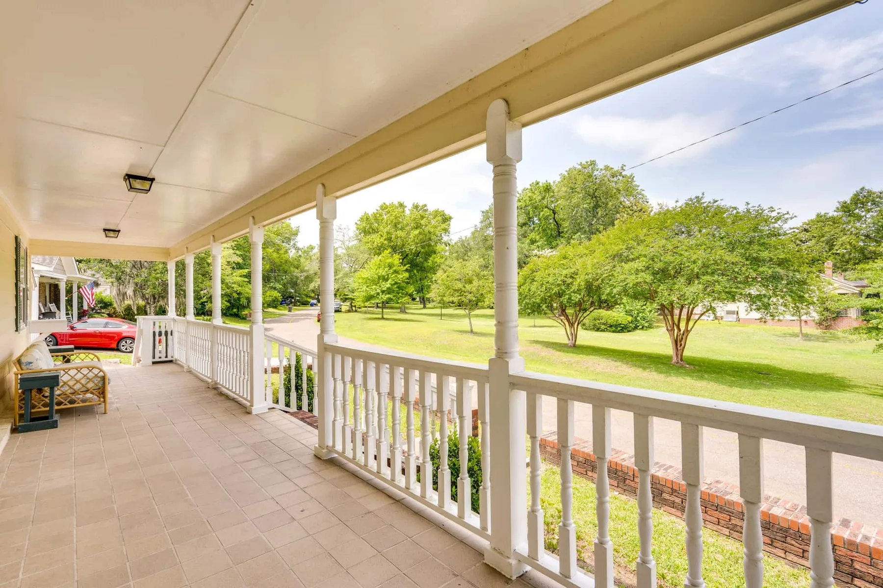 A covered porch with white railings overlooks a green lawn and trees.