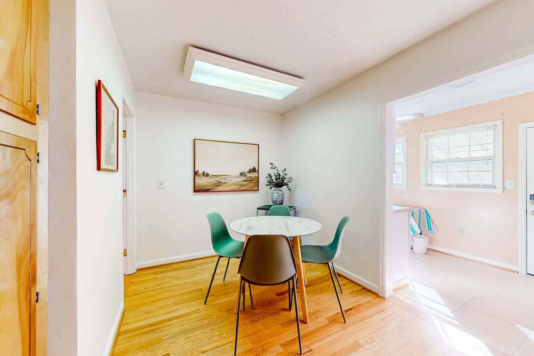 A dining area with a round table and chairs beside a bright adjoining room.