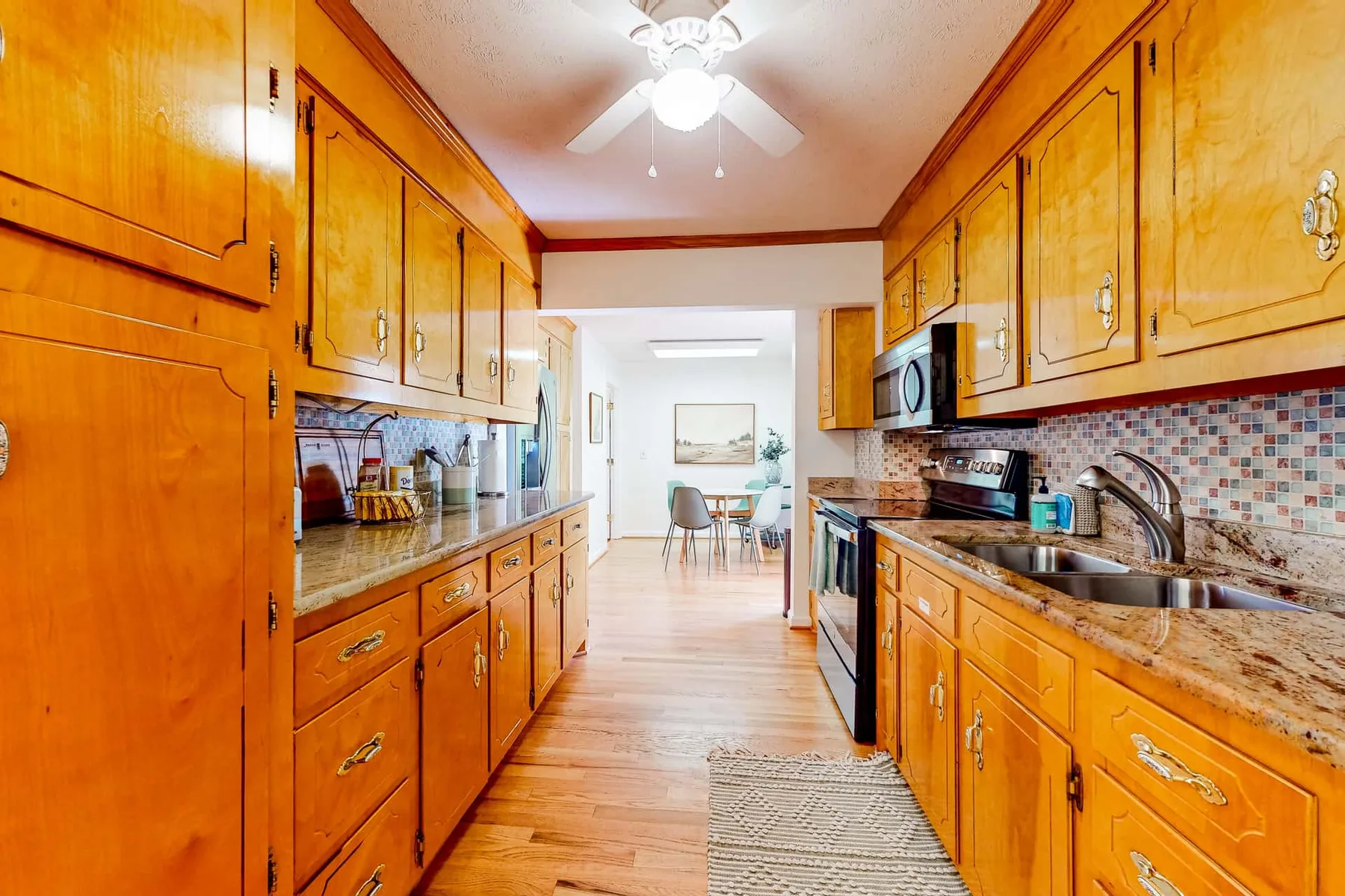 A kitchen with wooden cabinets, countertops, and a dining area visible beyond.