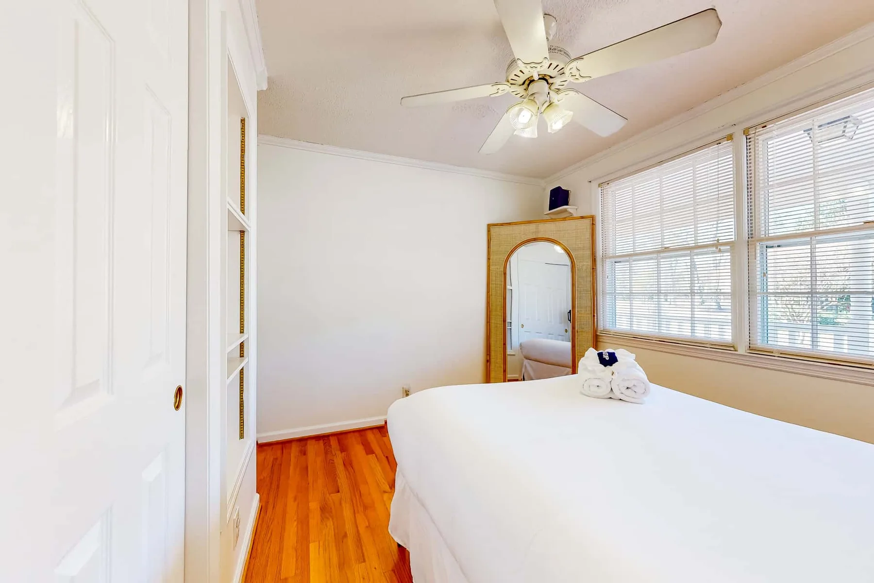 A bright bedroom with a bed, hardwood floor, and large windows.